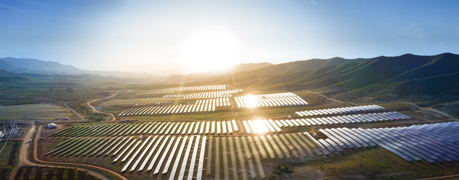 Solar plant from above with sun glare reflections on the photovoltaic panels and a bright glaring sun in the background.