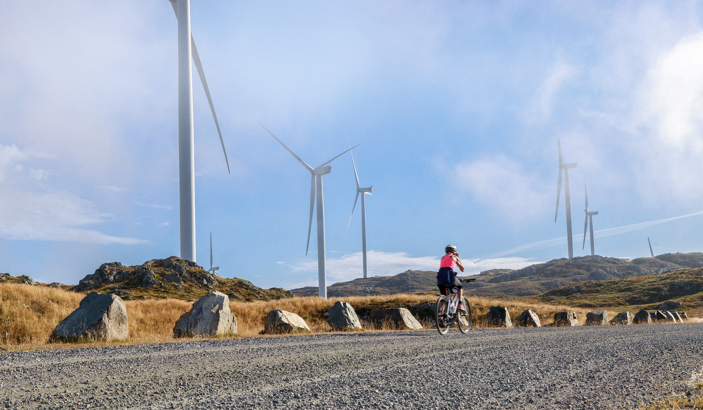 Woman cycling on gravel path with hills and windmills in background.