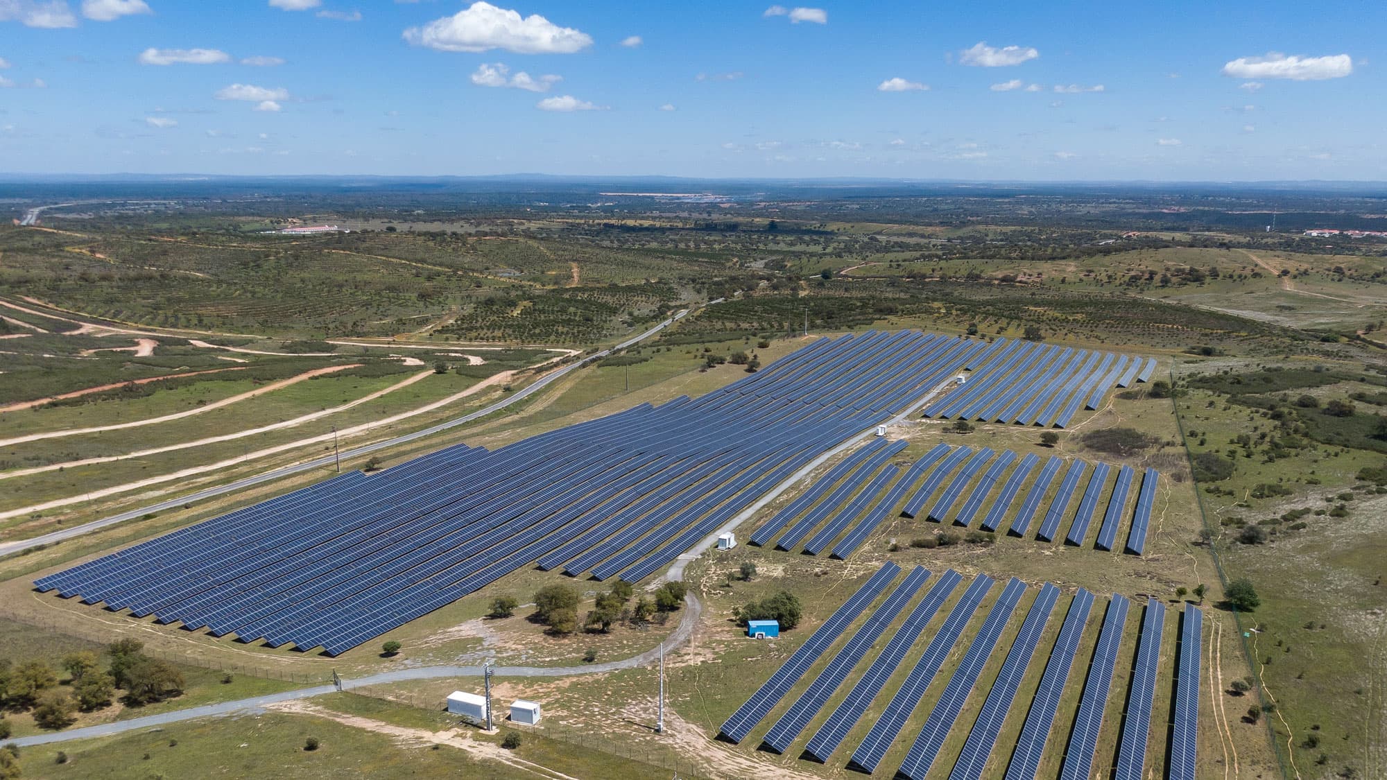 Solar energy plant in the middle of green pastures and slightly hilly landscape with blue sky.