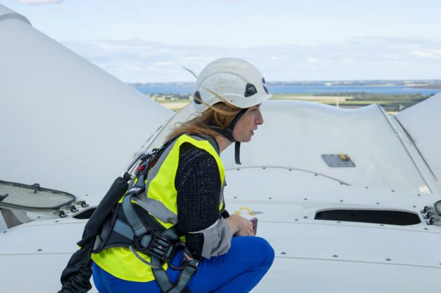 Kneeling woman in profile in yellow reflective vest on a windmill.