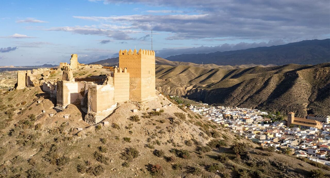 Castillo de Tabernas on a hill above spanish city near mountains and cloudy sky.