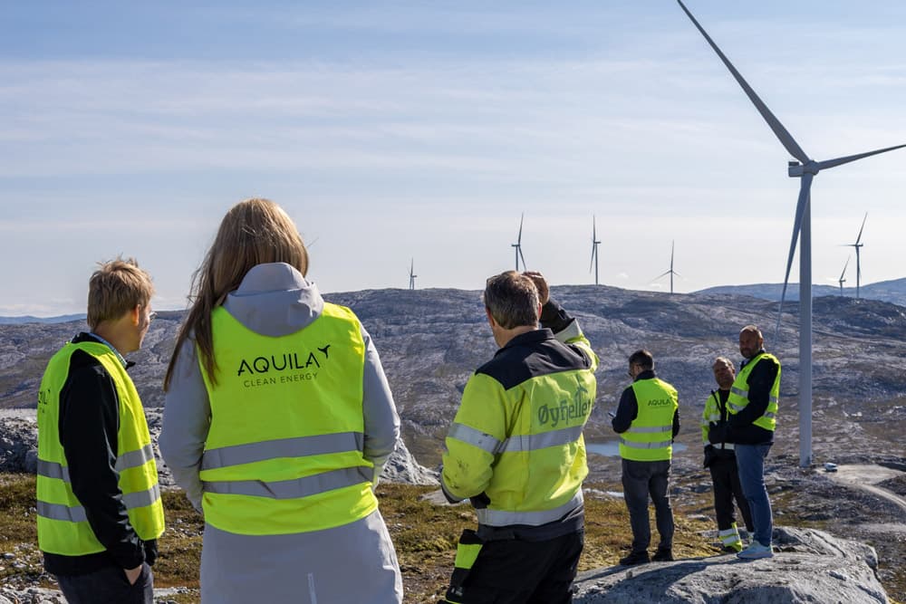 Six people talking in windmill park on rocky terrain and with blue sky.