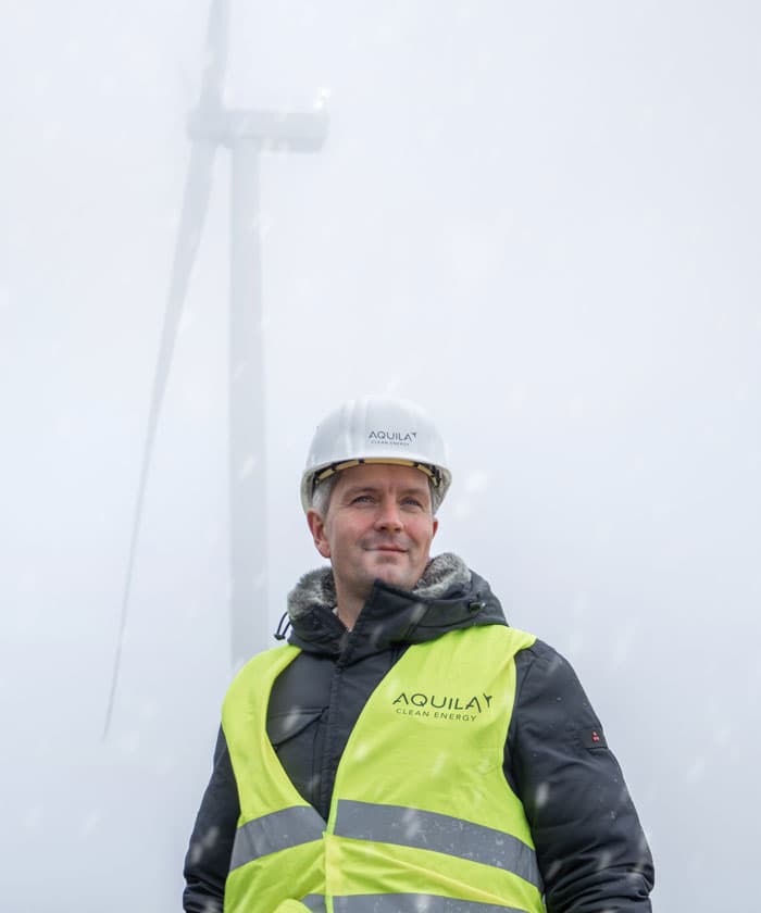 Man in reflective vest in front of a wind turbine while it is snowing heavily.