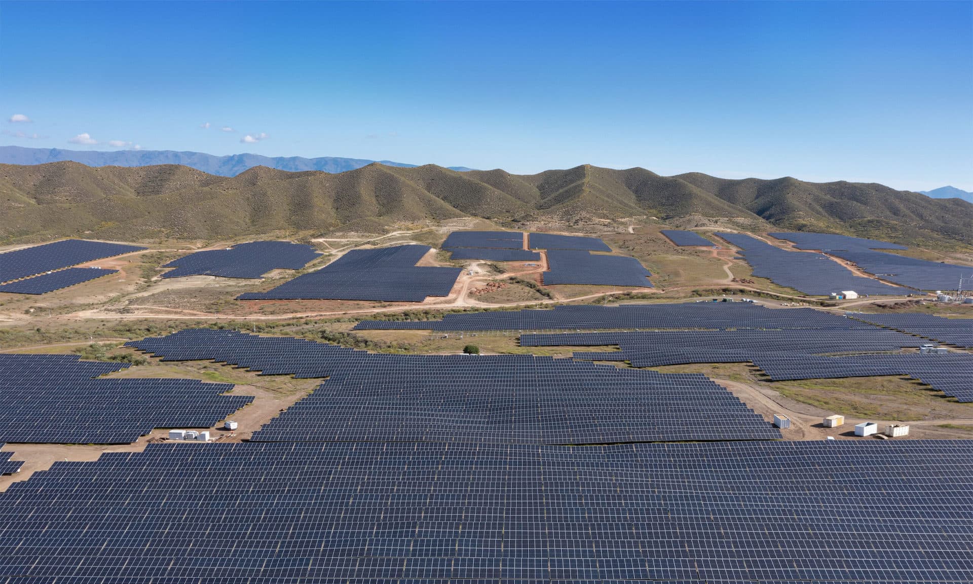 Solar plant from above with green mountains and blue sky in the background.