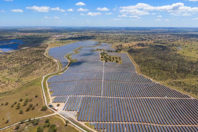 Solar energy plant in the middle of a wide green area with smaller bushes and lakes.