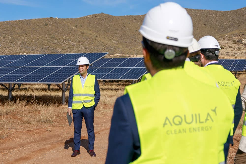 Three people in reflective vests and safety helmets on their heads talking to each other on a solar plant.